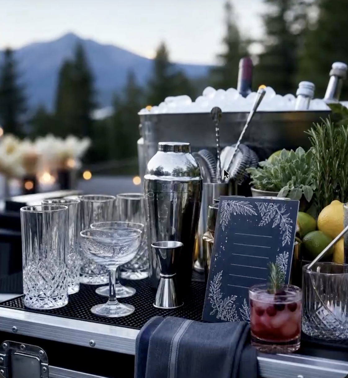 Prepared outdoor event bar with glassware, ice bucket, bottles, and cocktail ready for service